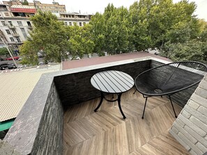 Une terrasse sur le toit, avec un plancher en bois, une table ronde et une chaise en fil de fer noir.
