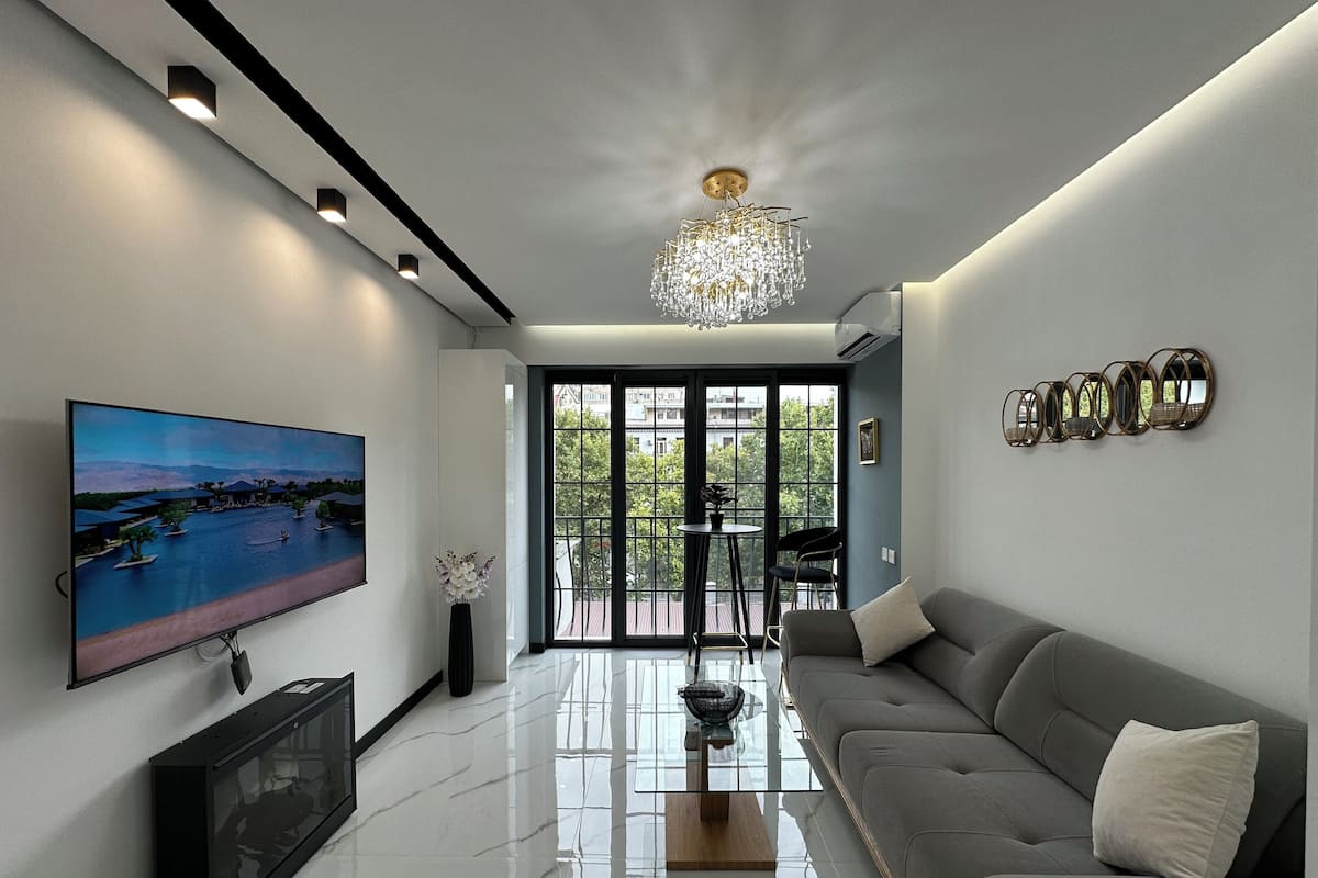 Uma sala de estar moderna com televisão de tela plana, sofá, mesa de centro e lustre.