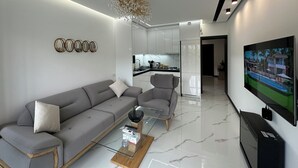 Una sala moderna con un sofá gris, una mesa de centro de cristal y un televisor montado en la pared.