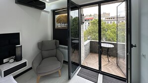 Una sala de estar moderna con un sillón gris, un televisor y un radiador. Cuenta con un amplio ventanal corredera que da a un balcón con un patrón de suelo tipo espiga.