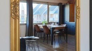 A dining area with a table, chairs, and a view of buildings through large windows. - "L'escale vers Bréhat" in Paimpol – Renovated Apartment in Port District (Paimpol)