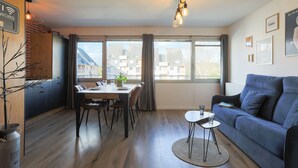 A modern living room with a dining area, large windows, and a view of buildings outside. - "L'escale vers Bréhat" in Paimpol – Renovated Apartment in Port District (Paimpol)