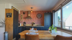 A kitchen with a brick wall, a wooden dining table, and a view of the outside. - "L'escale vers Bréhat" in Paimpol – Renovated Apartment in Port District (Paimpol)