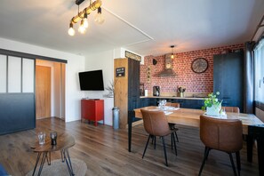 Cozinha moderna com parede de tijolos, área de jantar com mesa e cadeiras de madeira, e uma placa de bar.