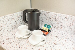 A kitchenette with a coffee maker, two cups, and a box of non-dairy creamer.