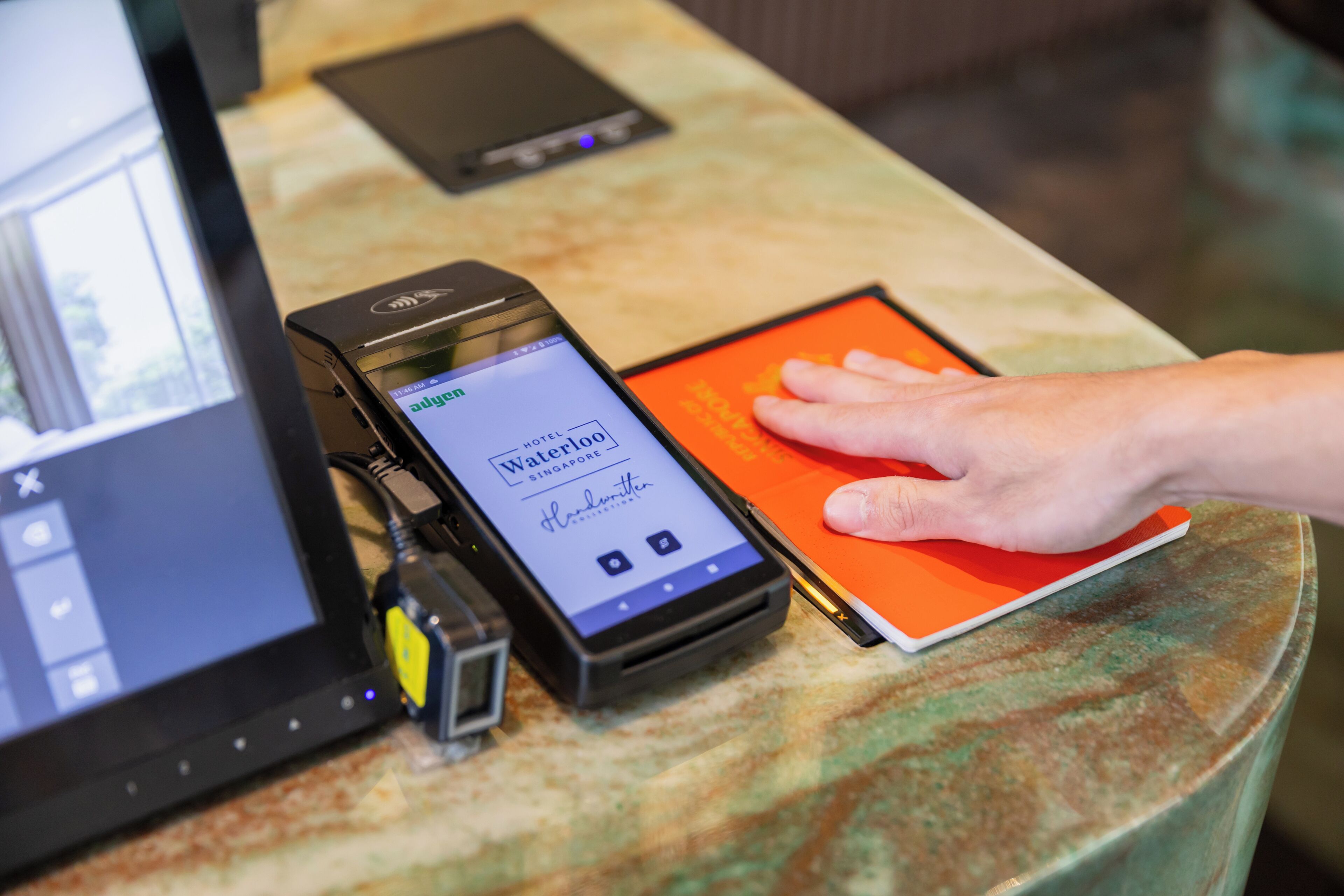 A smartphone displaying a hotel booking interface, a tablet, and a hand interacting with a red book on a table.