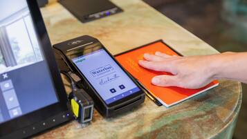 A smartphone displaying a hotel booking interface, a tablet, and a hand interacting with a red book on a table.