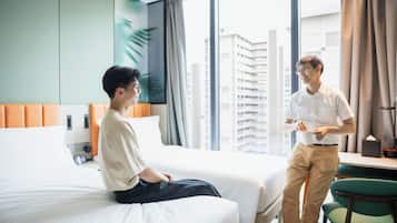 A hotel room with two beds, a desk, and a view of a cityscape.