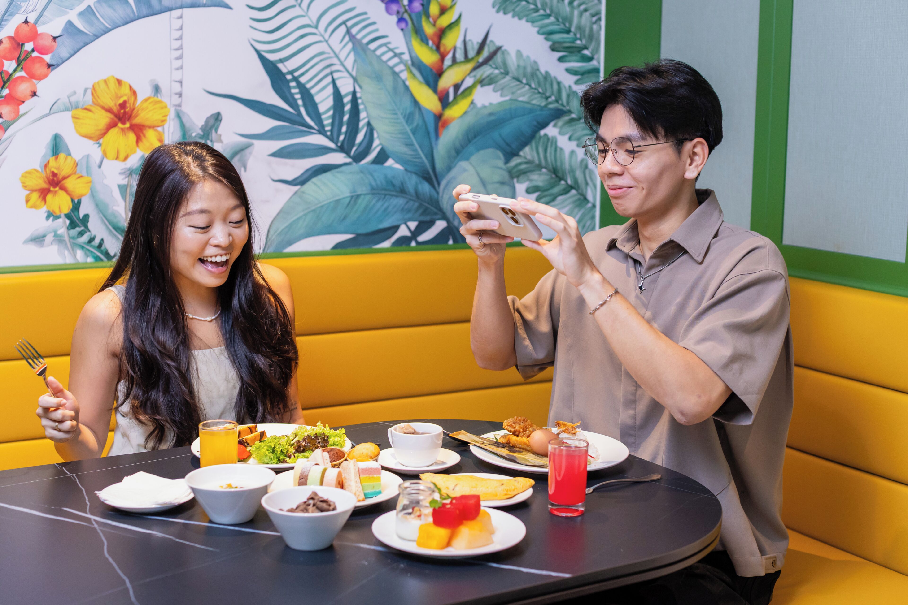 A dining area with a table set for two, featuring a variety of dishes and a colorful mural in the background.