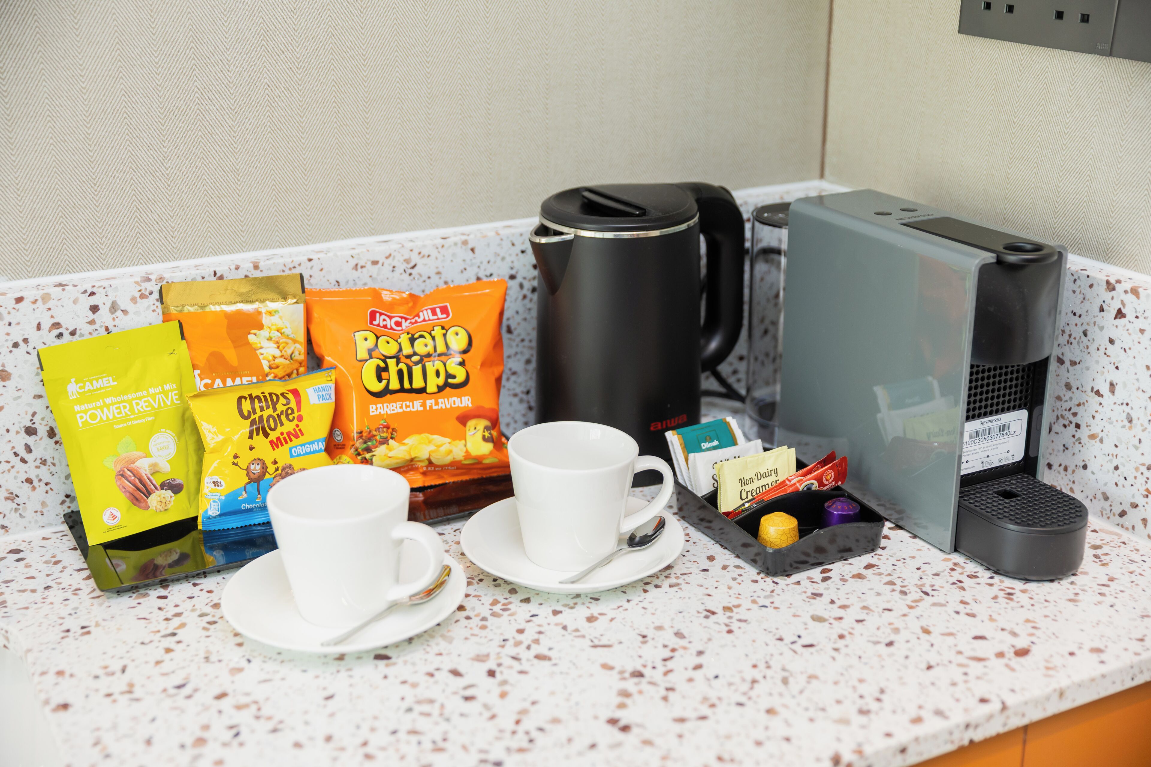 A breakfast setup with a coffee maker, a cup, and snacks on a speckled countertop.