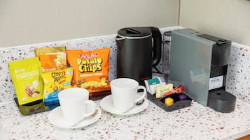 A breakfast setup with a coffee maker, a cup, and snacks on a speckled countertop.