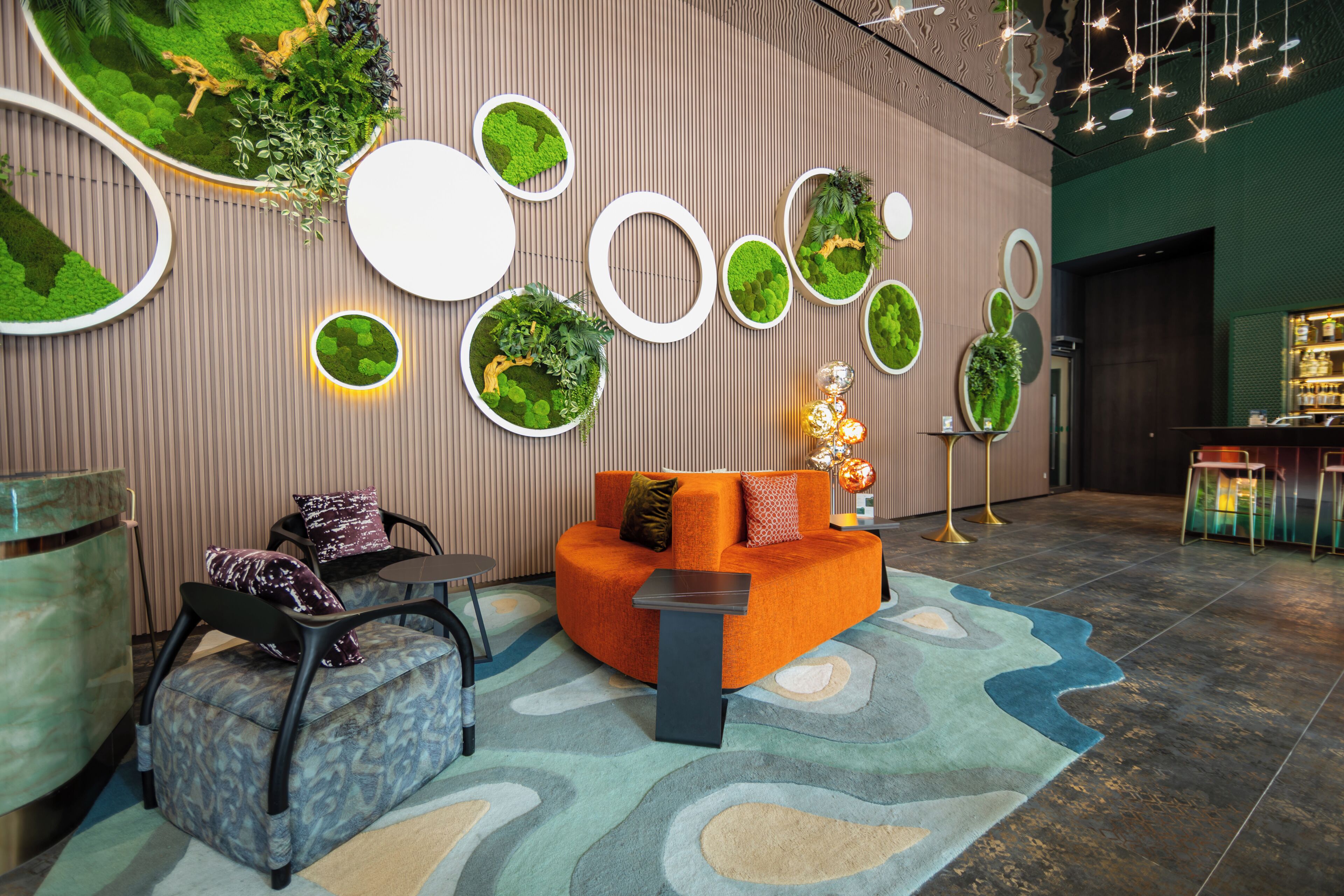 Un espace de détente moderne comprenant un canapé, des fauteuils, une petite table et des jardinières décoratives fixées au mur.