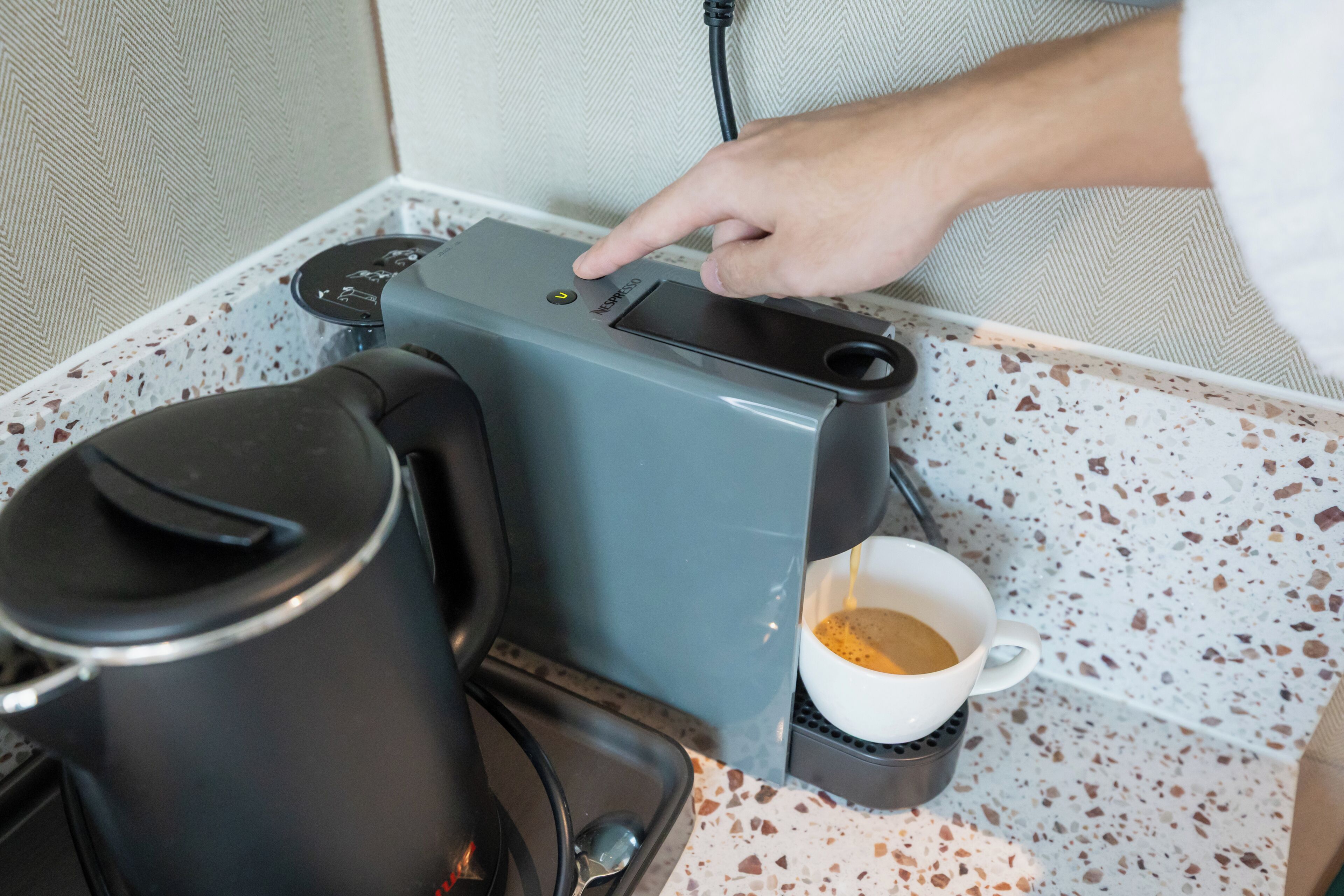 A coffee machine with a cup of coffee, a kettle, and a power cord plugged in.