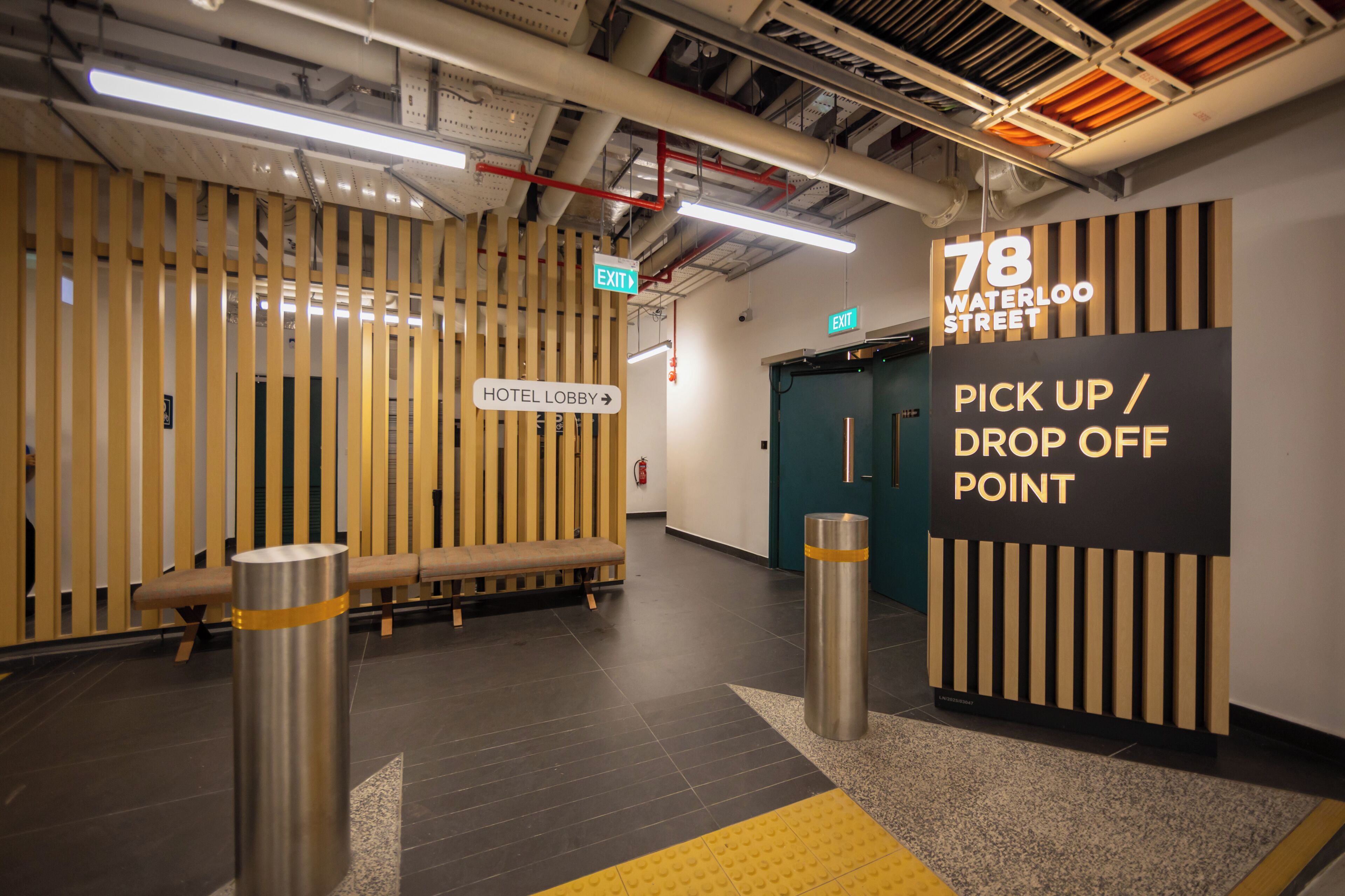 A hotel lobby with a wooden slat wall, a bench, a sign for the hotel lobby, and a pick-up/drop-off point sign.