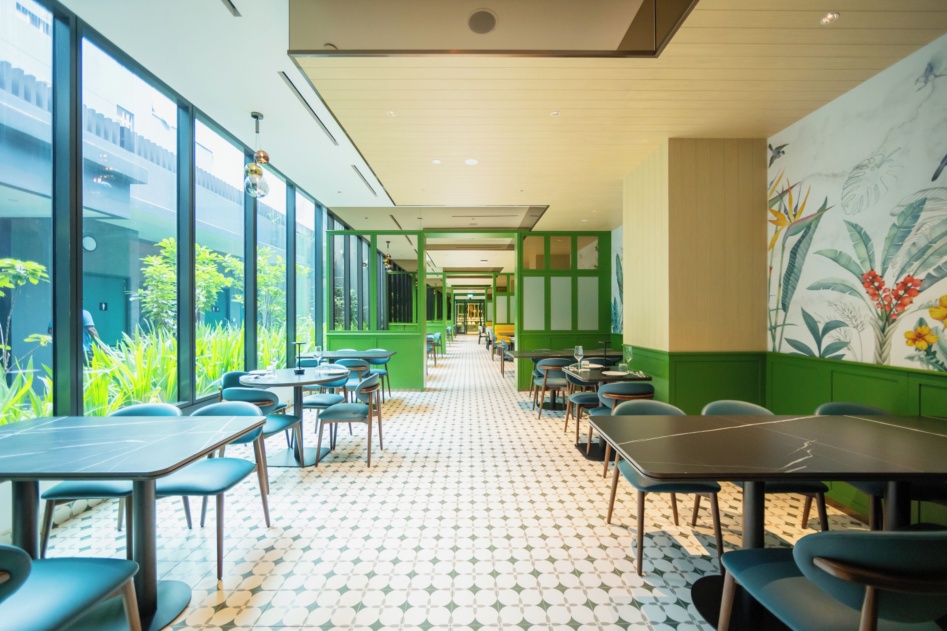 A modern restaurant with a long, narrow layout, green walls, and a patterned floor.
