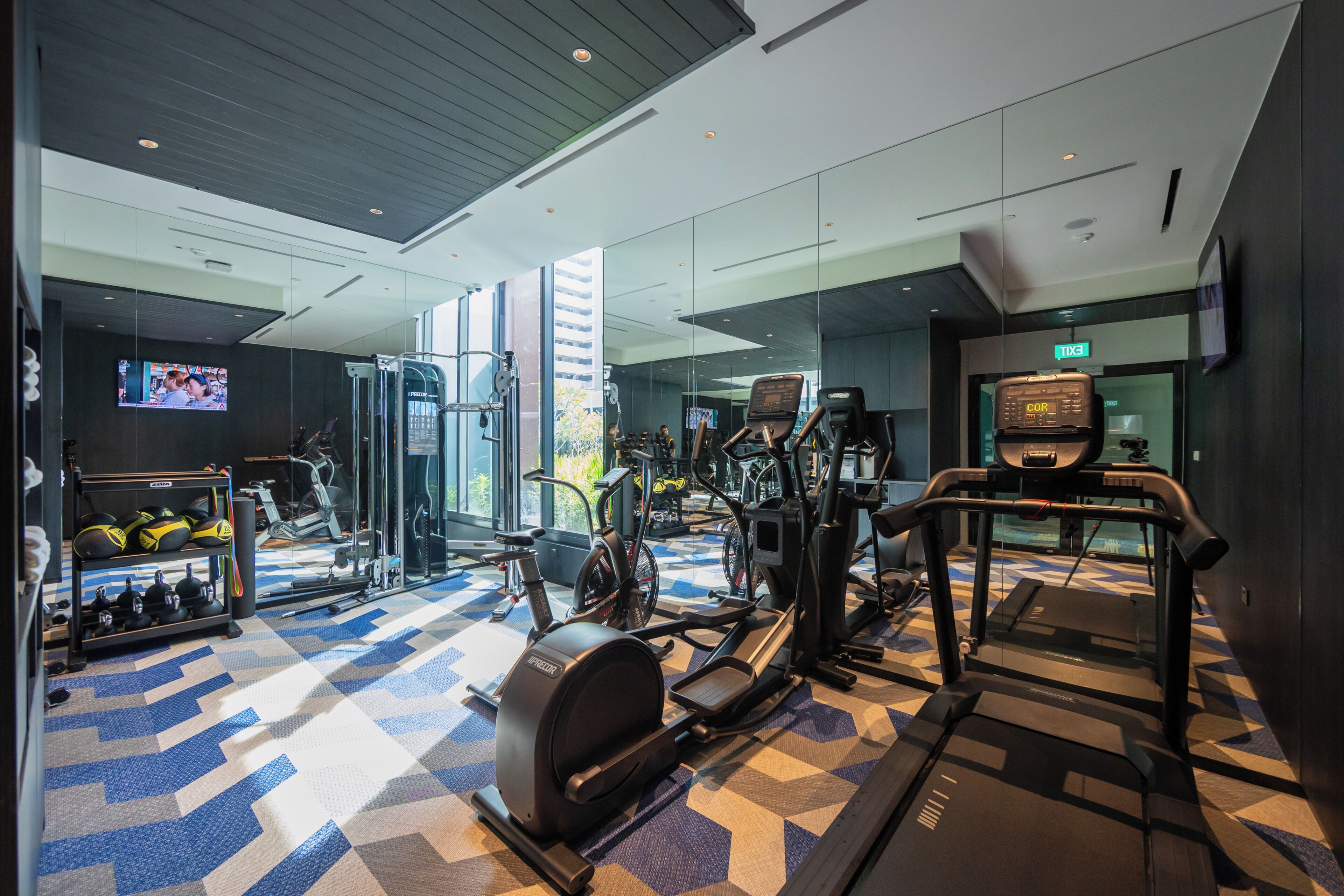 A modern gym with various exercise equipment, a large mirror, and a television screen.