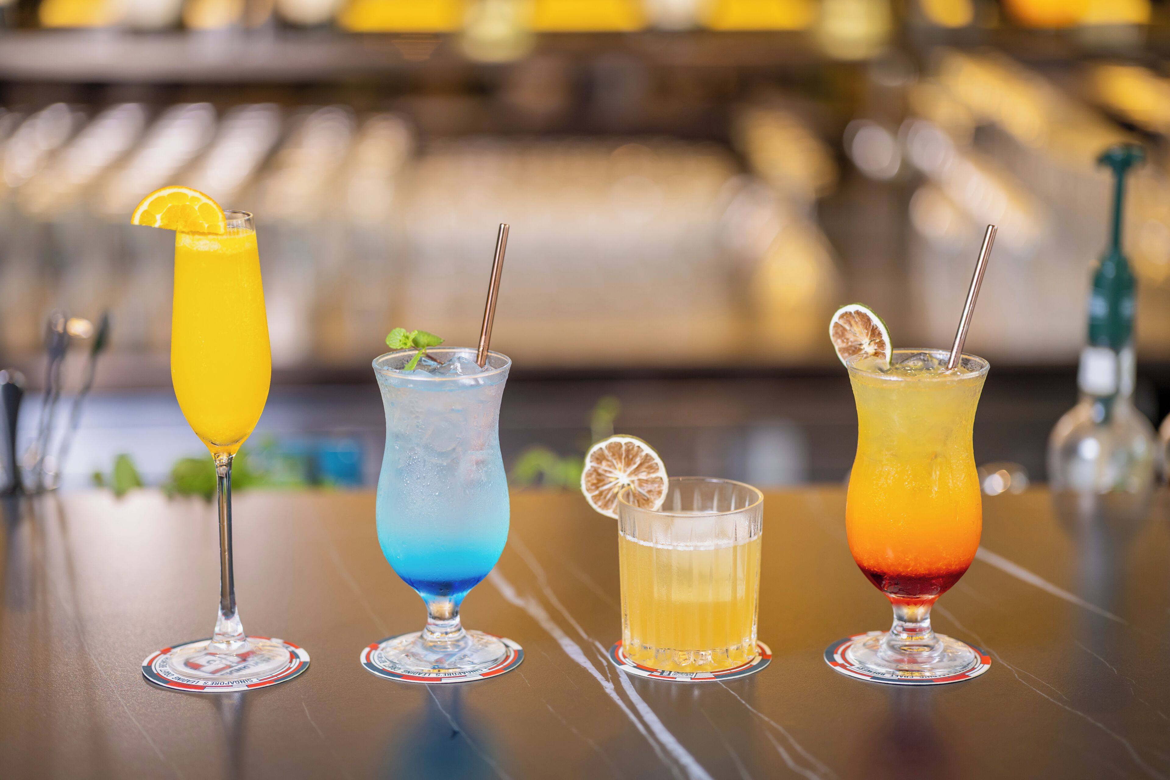 Four cocktails on a bar counter with a blurred background.