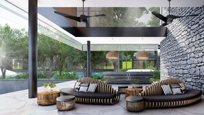 A modern outdoor seating area with a stone wall, wooden furniture, and ceiling fans. - Kamaliss MontAzure Phuket - MGallery Collection (Kamala)