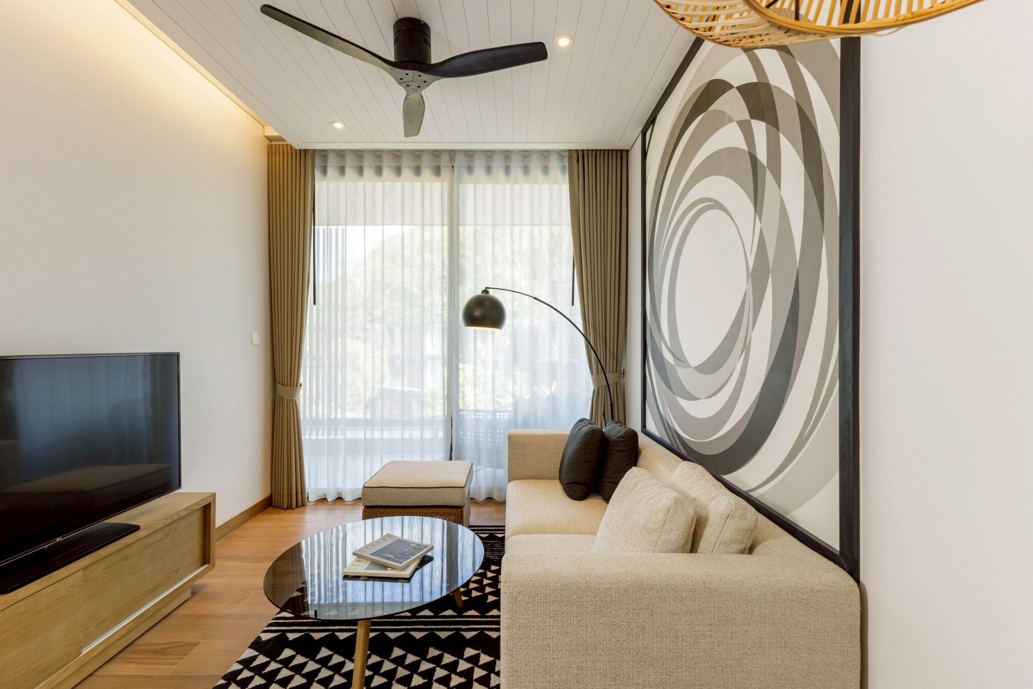 A modern living room with a flat-screen TV, a round coffee table, a sofa, and a large abstract wall art piece.