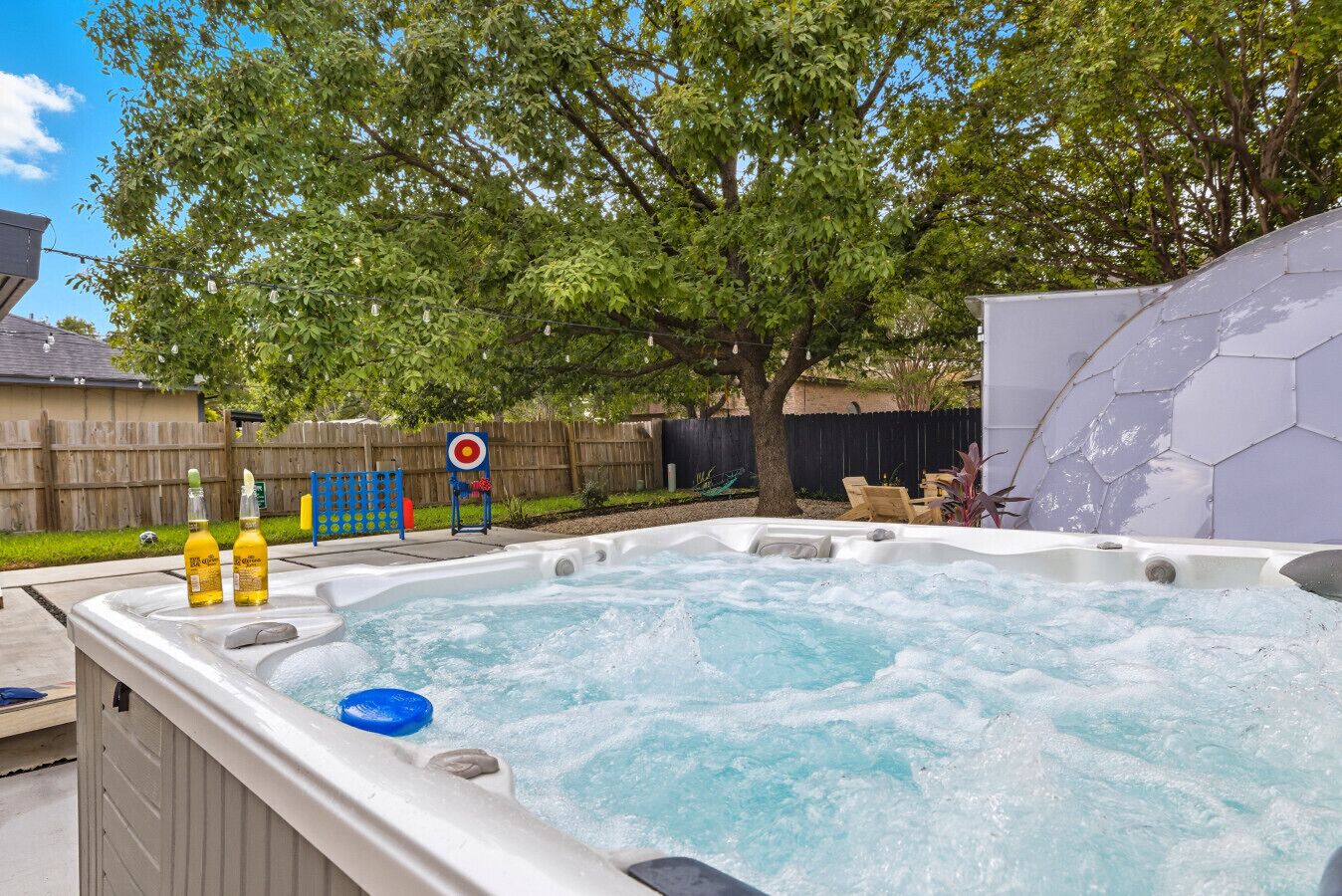 A hot tub in a backyard with a wooden fence, a tree, and a hexagonal wall.