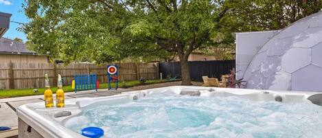 A hot tub in a backyard with a wooden fence, a tree, and a hexagonal wall.