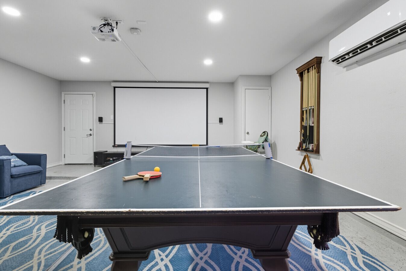 Una habitación con mesa de ping pong, proyector y sofá azul.