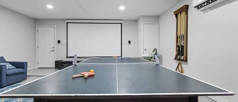Una habitación con mesa de ping pong, proyector y sofá azul.