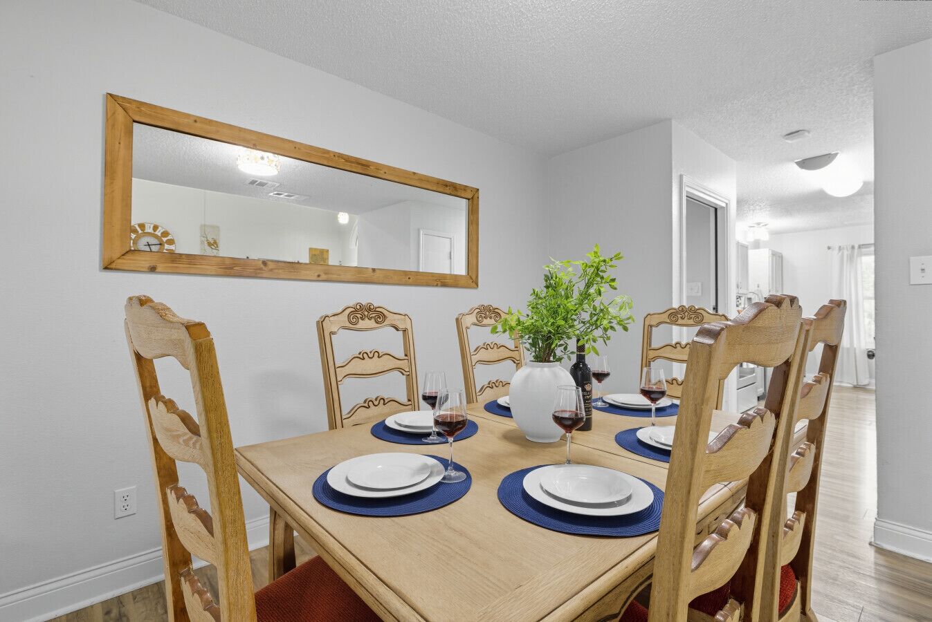 A dining room with a wooden table, six chairs, a mirror, and a vase with a plant.