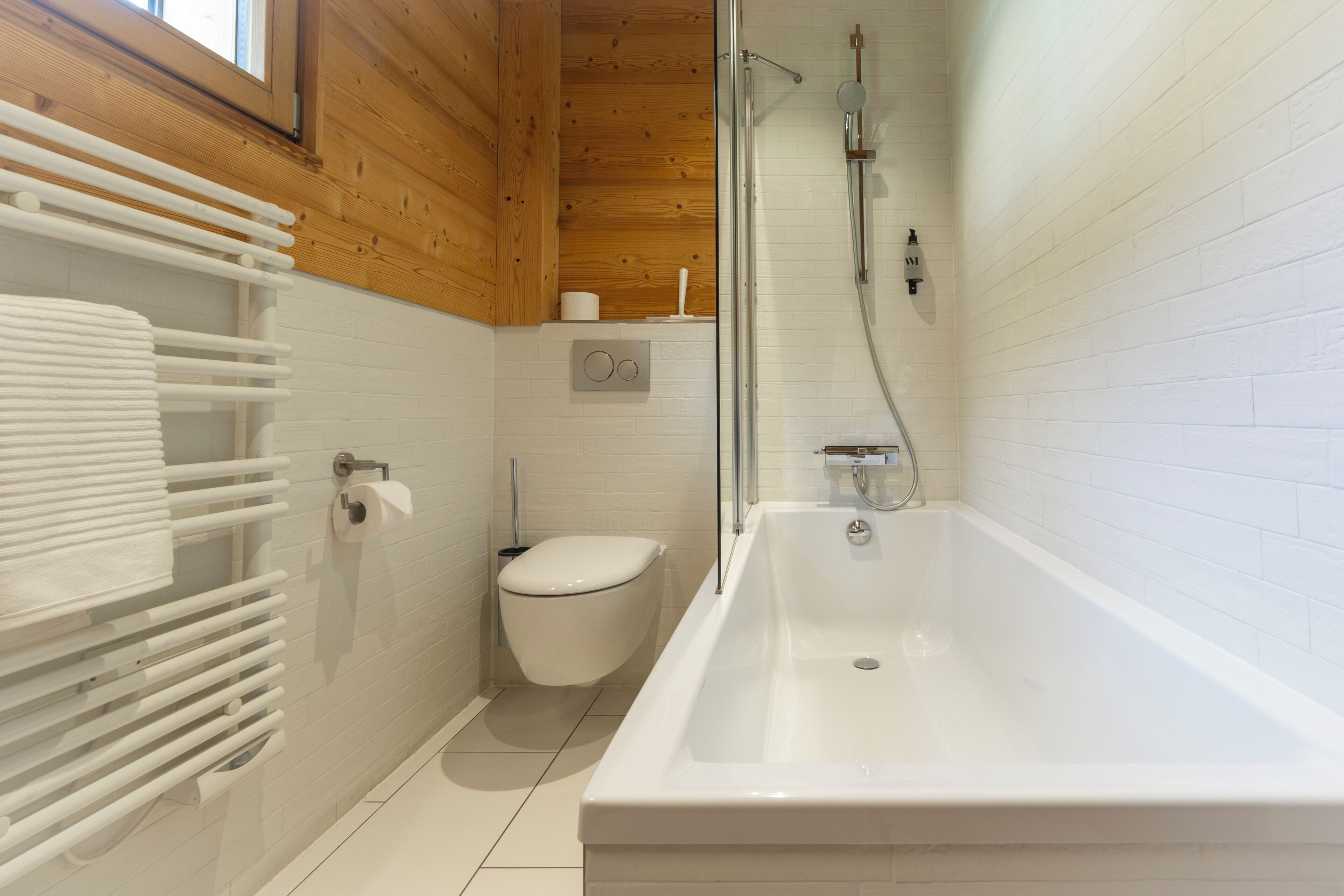 A modern bathroom with a white bathtub, a toilet, and a towel rack.