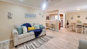 Een woonkamer met een bank, een vloerkleed en een eethoek met stoelen en een tafel.