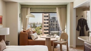 Une chambre d’hôtel comprenant un lit, un canapé, une table à manger, une chaise, une lampe, une vue sur le paysage urbain et un peignoir accroché au mur.