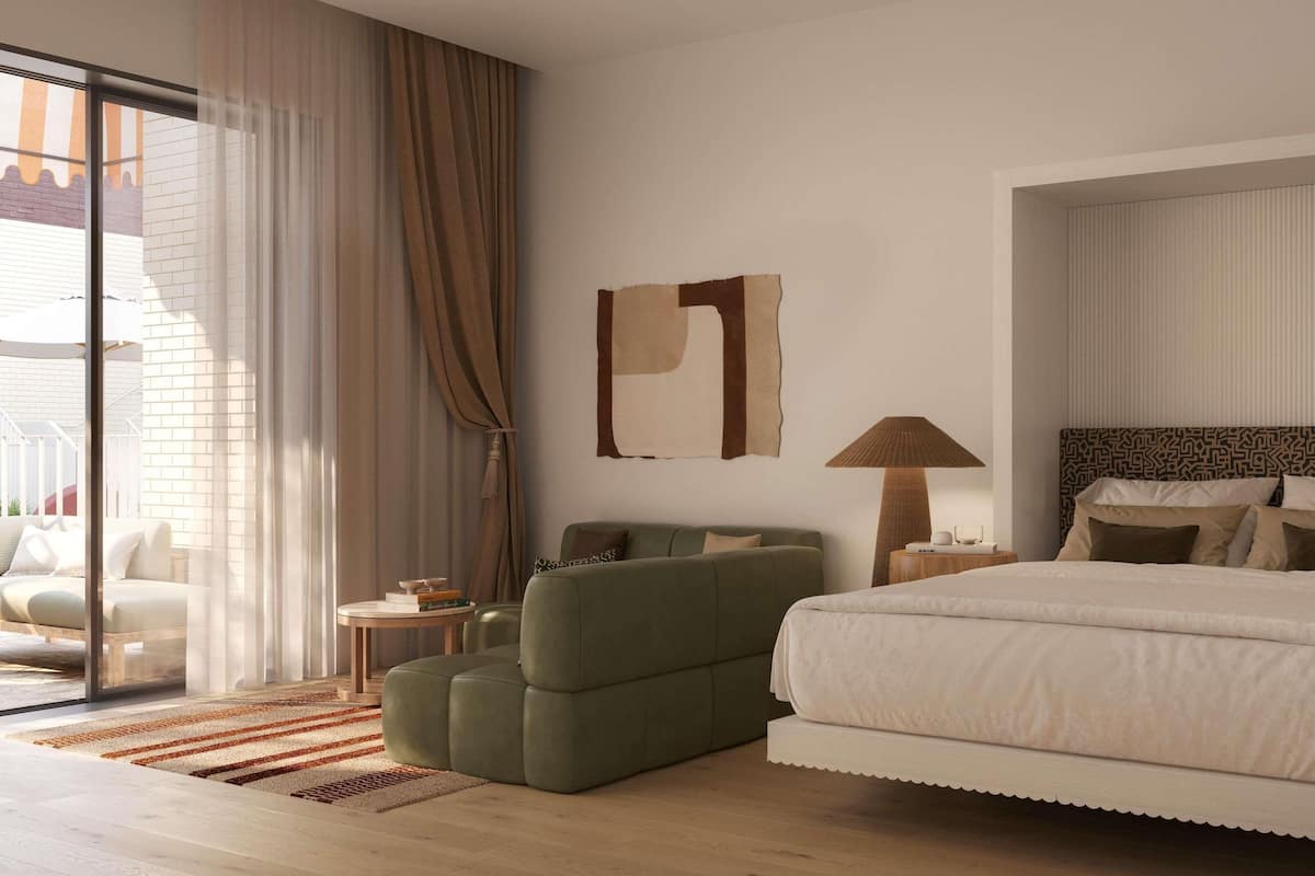 A modern hotel room with a large bed, a green armchair, a small side table, and a large window with curtains.