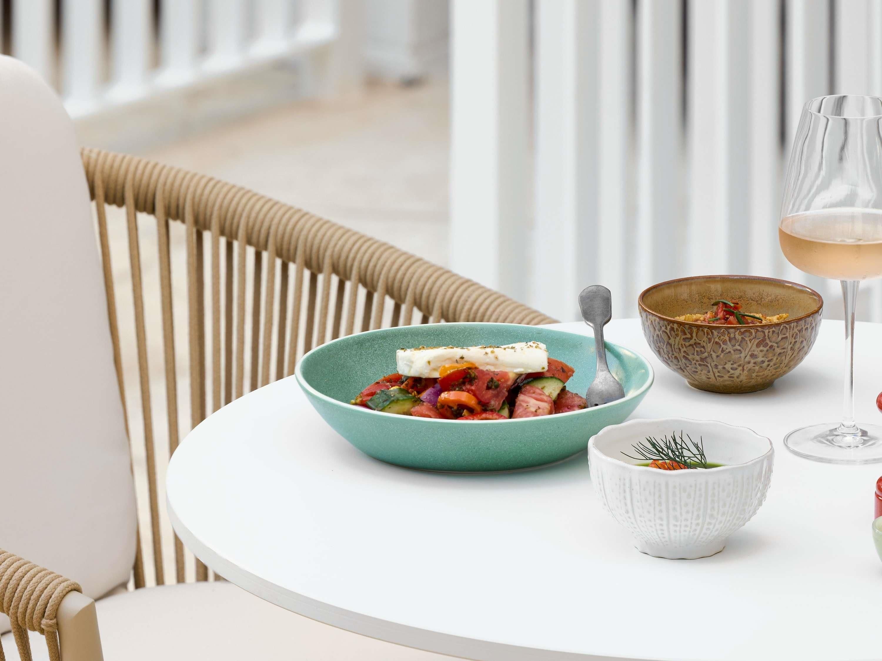 A dining table with a bowl of salad, a glass of drink, and a decorative bowl.