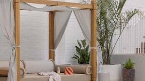 A wooden canopy bed with a beige mattress, a white curtain, and a pair of slippers on the floor. - Hyde Perth (Perth)