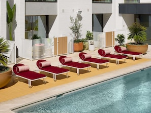 A poolside area with sun loungers, potted plants, and a modern building with large windows. - Hyde Perth (Perth)