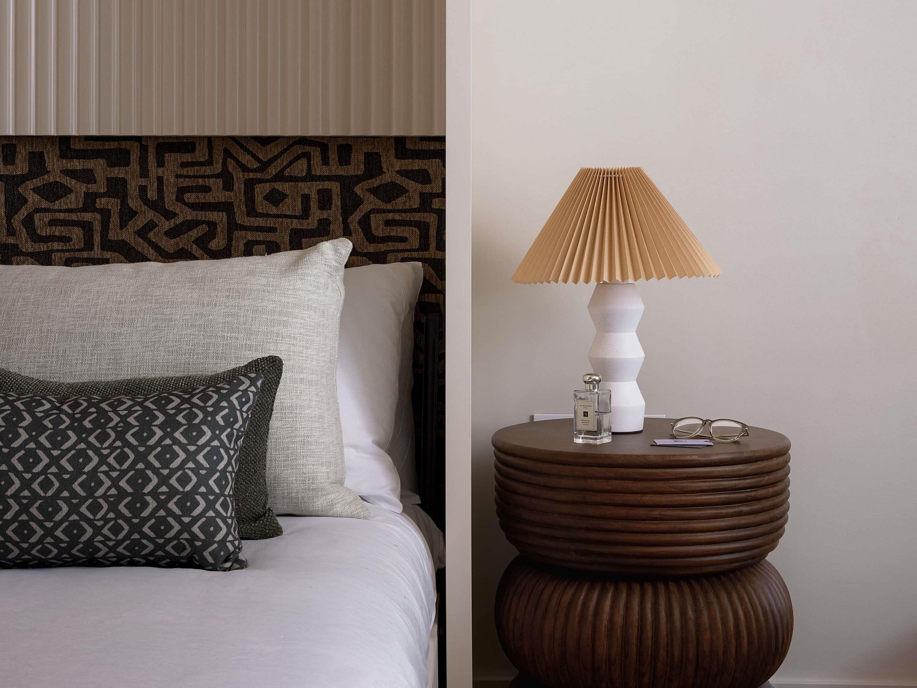 Un lit bien fait, agrémenté d’oreillers à motifs, une lampe moderne et une petite table avec des verres et une bouteille.