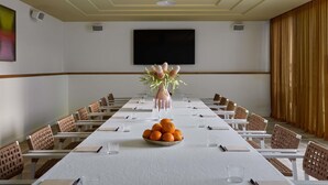 Een vergaderruimte met een lange tafel, stoelen, een televisietoestel en een decoratieve plant.