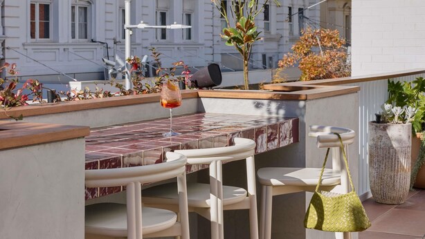 Une terrasse sur le toit avec un espace bar, des sièges en plein air et une vue sur un bâtiment de style classique.