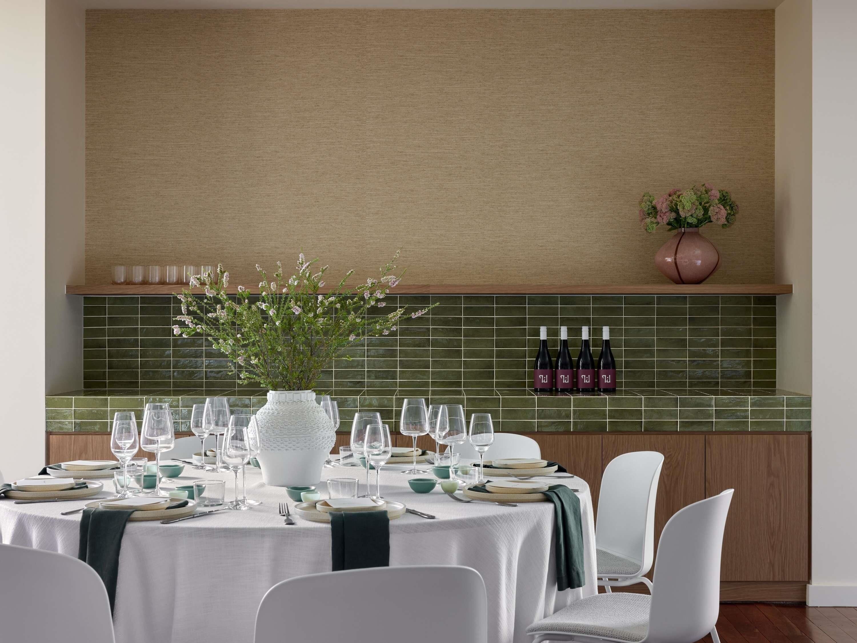 A dining area with a table set for four, a vase with flowers, and wine bottles on the wall.