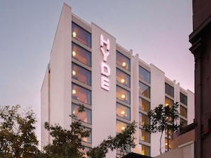Un hotel de varios pisos con un llamativo letrero de neón que dice 'HYDE' en la fachada.