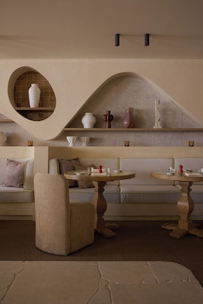 A dining area with a round table, a cushioned bench, and a wall-mounted shelf with decorative vases.