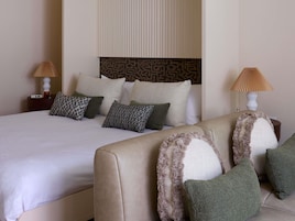 A hotel room with a bed, a sofa, patterned pillows, and two bedside lamps.
