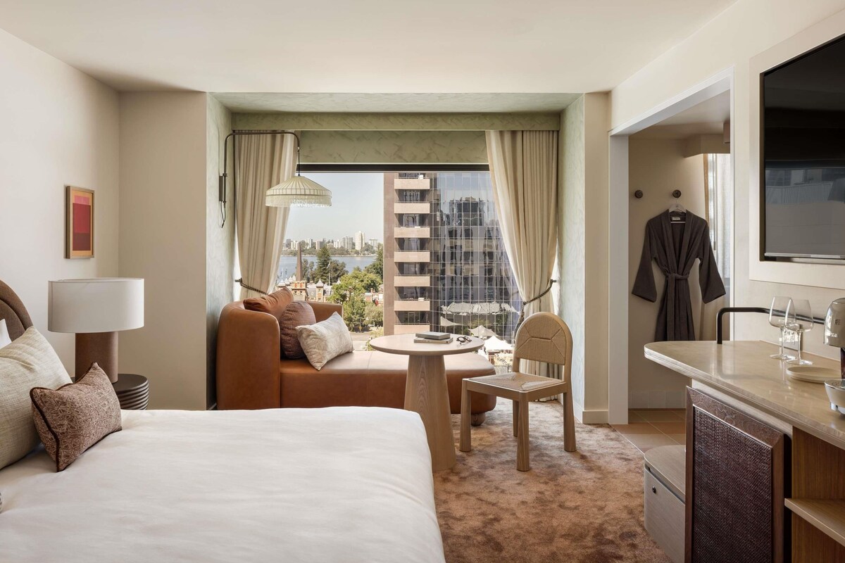 A hotel room with a bed, a sofa, a dining table, a chair, a robe, and a TV.