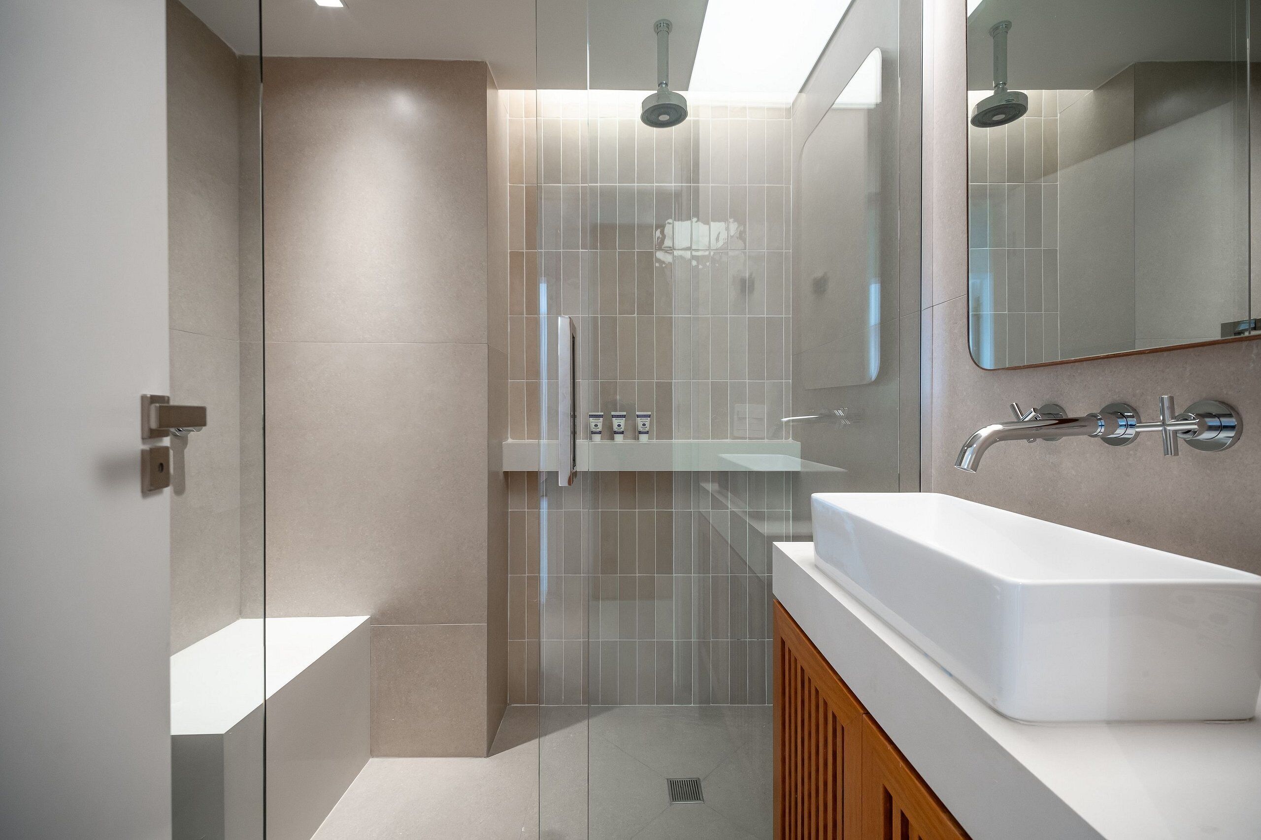 Un bany modern amb una cabina de dutxa de vidre, un lavabo blanc i un mirall sobre el lavabo.