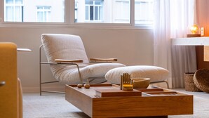 Ein modernes Wohnzimmer mit großem Fenster, einer Couch, einem Couchtisch aus Holz mit Dekoration und einer kleinen Lampe auf einem Beistelltisch.