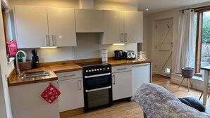 A modern kitchen with white cabinets, a black stove, and a wooden countertop. - Gosfield Cartlodge Retreat (Halstead)