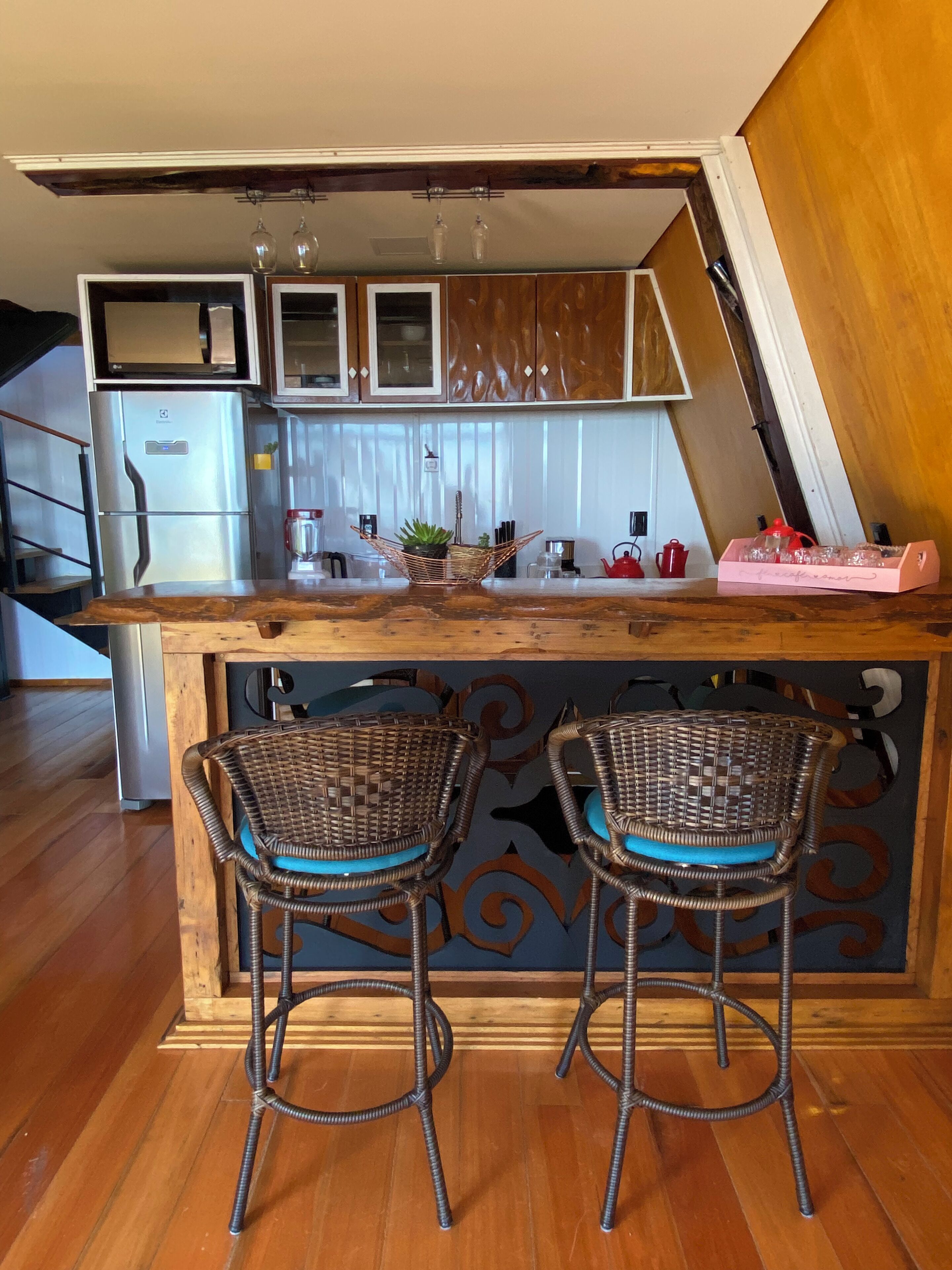 A kitchen with a wooden counter, two wicker bar stools, a stainless steel refrigerator, and a hanging light fixture.