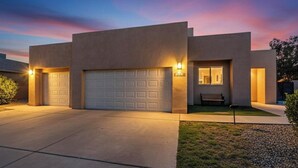 A modern two-story house with a garage, a well-lit entrance, and a small patio area. - Beautiful North Valley home, garage, yard, BBQ (Albuquerque)