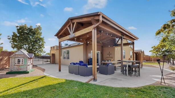 A covered outdoor seating area with a wooden structure, a small playhouse, and a patio table and chairs. - Beautiful North Valley home, garage, yard, BBQ (Albuquerque)