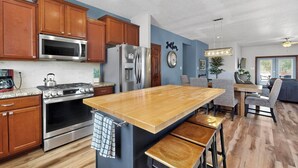 A modern kitchen with wooden cabinets, stainless steel appliances, and a central island with bar stools. - Beautiful North Valley home, garage, yard, BBQ (Albuquerque)